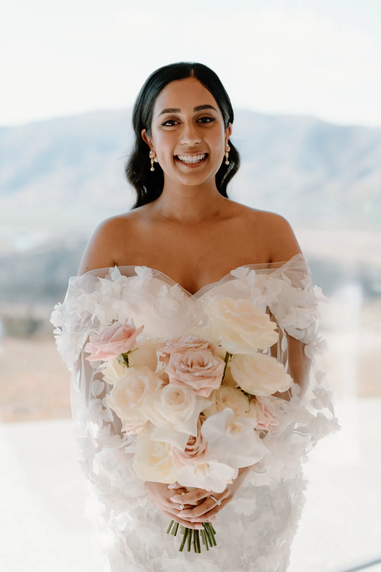 Bride with dark, sleek side-parted waves and a blush rose bouquet