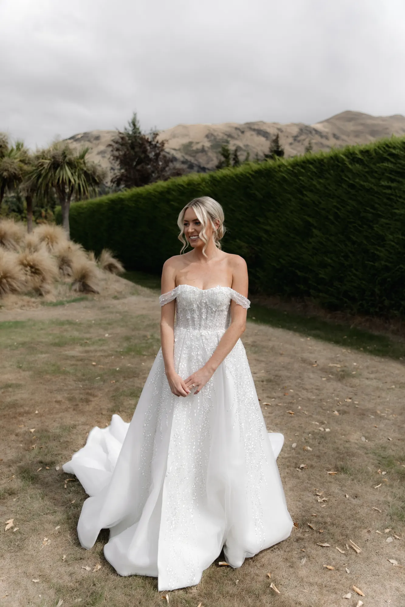 Bride in a sparkly off-shoulder gown with a soft textured updo and face-framing tendrils